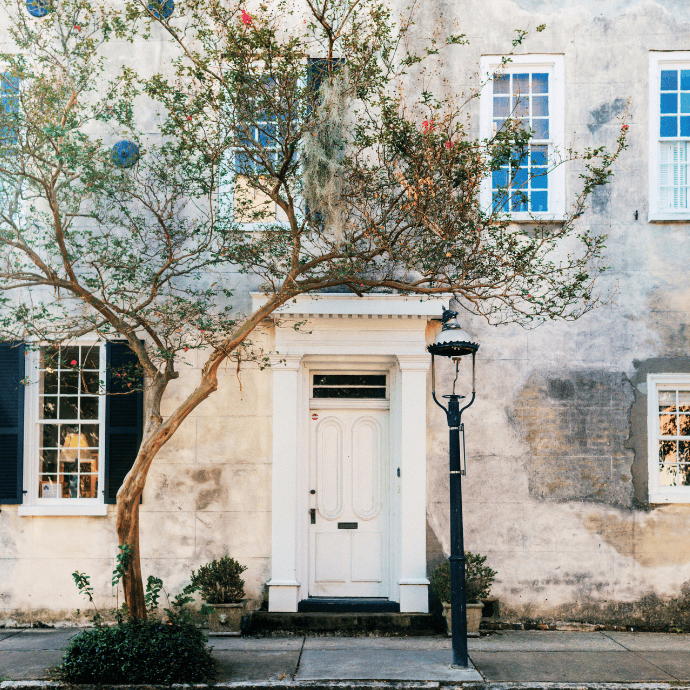 Charming white door with vintage street lamp and flowering tree in front of rustic building.