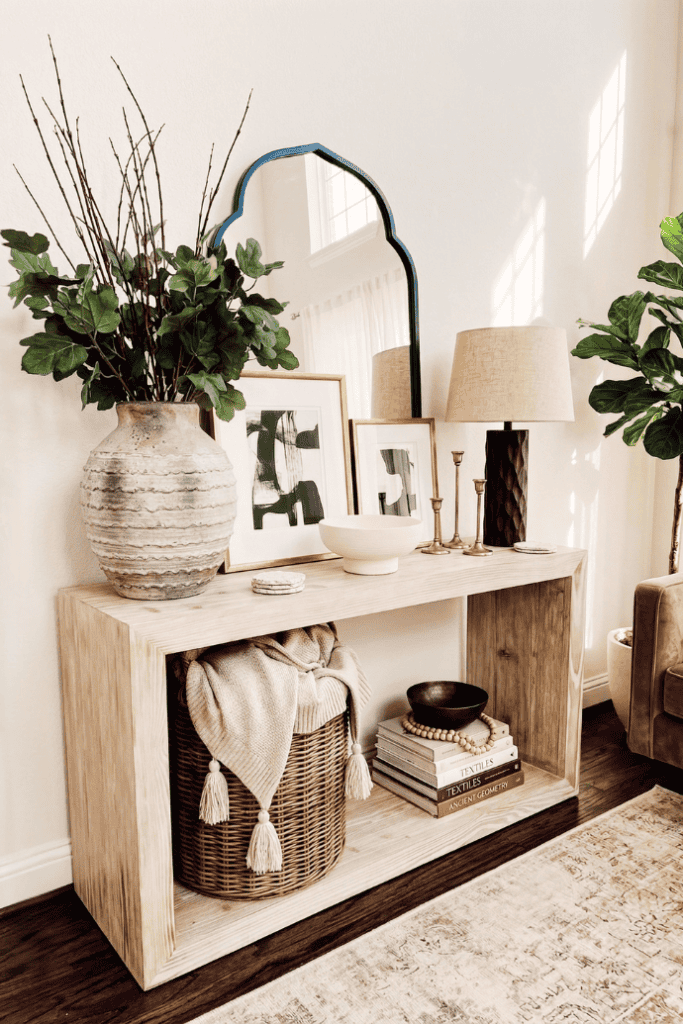 A lush decorative console table styled with plants, artwork, and accessories in a bright living room.