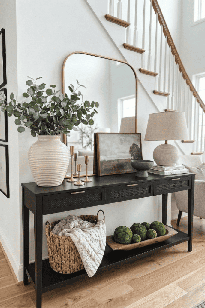 A lush green plant in a beige vase on a black console table with decorative items in a bright living.