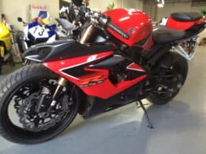 A red and black sport motorcycle is parked indoors, exuding a sleek design that would impress even a performance coach. In the background, a blue motorcycle and a Red Bull sign add to the dynamic scene, all set against the cool solidity of a concrete floor.