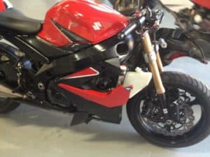 A red and black Suzuki motorcycle, Clay Green's choice for flow and performance, is parked indoors. It showcases a sleek design and detailed bodywork, with the front wheel and suspension prominently visible, focusing on the bike's sporty, aerodynamic styling.