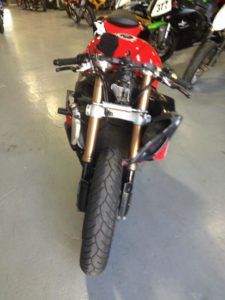 In the showroom, a red motorcycle stands out with its striking rear view, showcasing impeccable suspension and visible handlebars. The attention to detail extends to the tire and rear frame, echoing the precision one might expect from Clay Green’s expertise as a flow and performance coach.