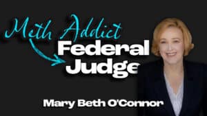 Mary Beth O'Connor, with short blonde hair, wearing a dark blazer and white blouse, stands next to bold text reading "Meth Addict → Federal Judge" and "Mary Beth O'Connor," highlighting her inspiring story of addiction recovery on a black background.