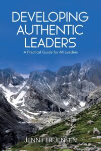 Book cover for "Developing Authentic Leaders" by Jennifer Jensen, featuring a mountainous landscape with snow, rocky peaks, and greenery under a blue sky. Subtitle: "A Practical Guide for All Leaders." Explores vulnerability in leadership and growth.
