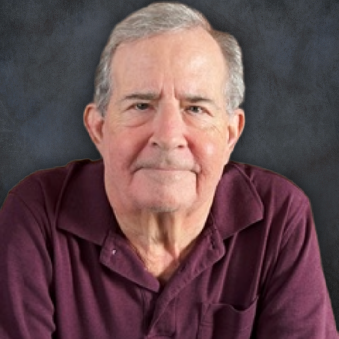 An older man with gray hair, wearing a maroon collared shirt, sits in front of a dark textured background, looking directly at the camera with a slight smile—embodying gratitude and resilience strategies when life gets hard.
