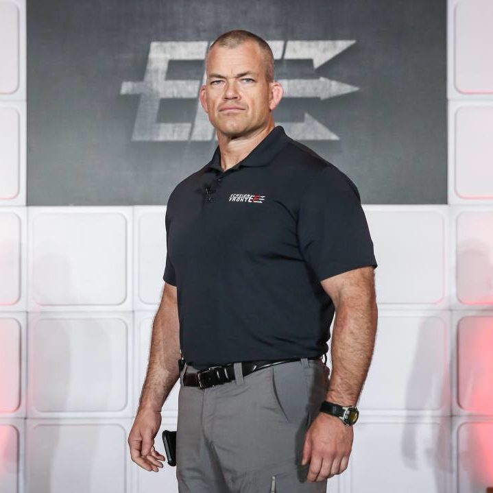 A man in a black polo shirt and gray pants stands confidently on stage, embodying the principles of "The Dichotomy Of Leadership". Behind him, a logo and white paneling add to the authoritative ambiance. The letters "EEF" subtly mark the bottom right corner.