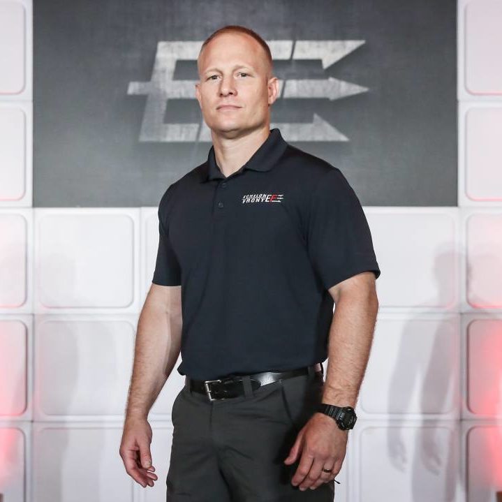 A person in a black polo shirt stands confidently, embodying the essence of "The Dichotomy Of Leadership," in front of a stylized logo on a striking white and red backdrop.