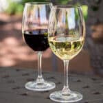 Two elegant wine glasses, one filled with red wine and the other with white wine, placed on a table in a scenic outdoor setting.