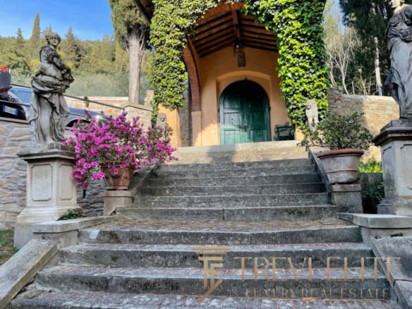 Роскошные ступеньки и статуи у входа в исторический особняк с зелёной дверью, окружённые цветущими растениями на территории элитной недвижимости в Италии.