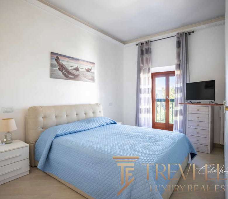 Уютная спальня с большой кроватью, светлыми стенами и видом на балкон. Современный интерьер, свежие ткани и простор создают комфорт и роскошь для жильцов.