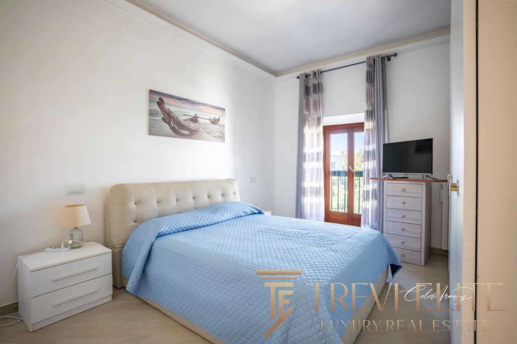 Уютная спальня с большой кроватью, светлыми стенами и видом на балкон. Современный интерьер, свежие ткани и простор создают комфорт и роскошь для жильцов.