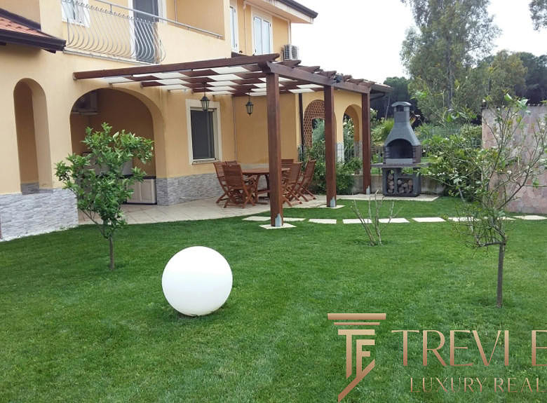 Красивый ухоженный двор с зоной барбекю и зеленой травой, окруженный деревьями и уютной террасой, идеально подходит для отдыха и проведения мероприятий.