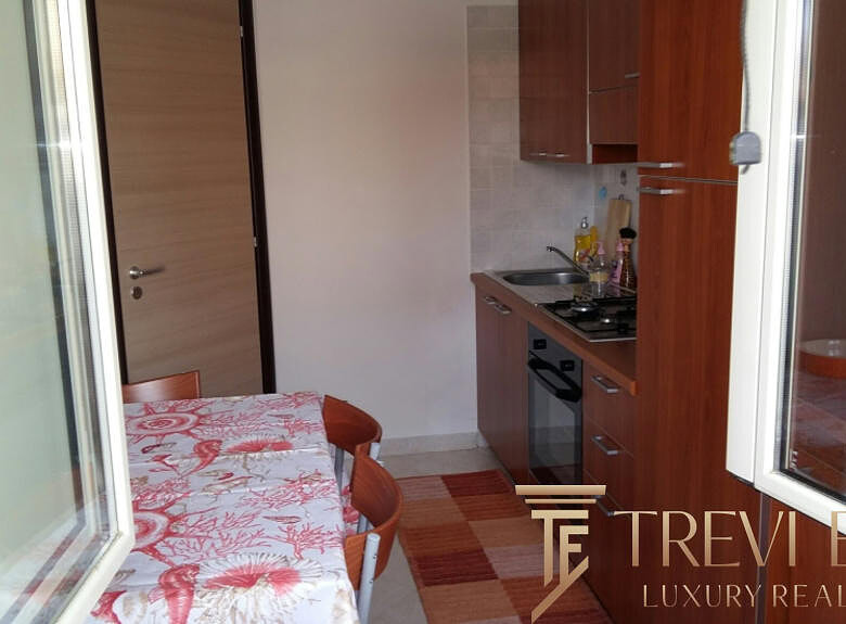 Миниатюрная кухня с деревянными шкафами и обеденным столом в светлой квартире на фоне окна.