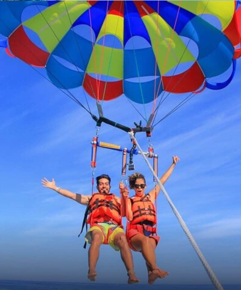 Punta Cana Two people parasailing over the ocean with colorful parachute.