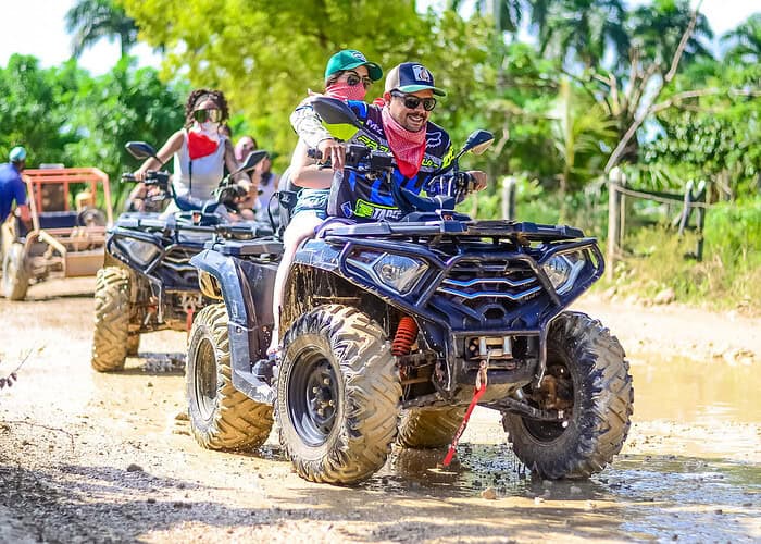 Punta Cana Group of people riding ATV quads through muddy terrain in Punta Cana, Dominican Republic.