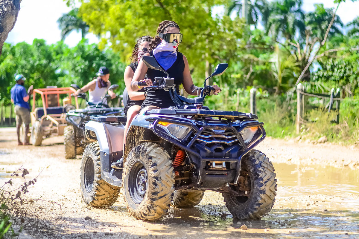 Punta Cana Two women riding a black ATV through a muddy trail in a lush tropical setting in Punta Cana.