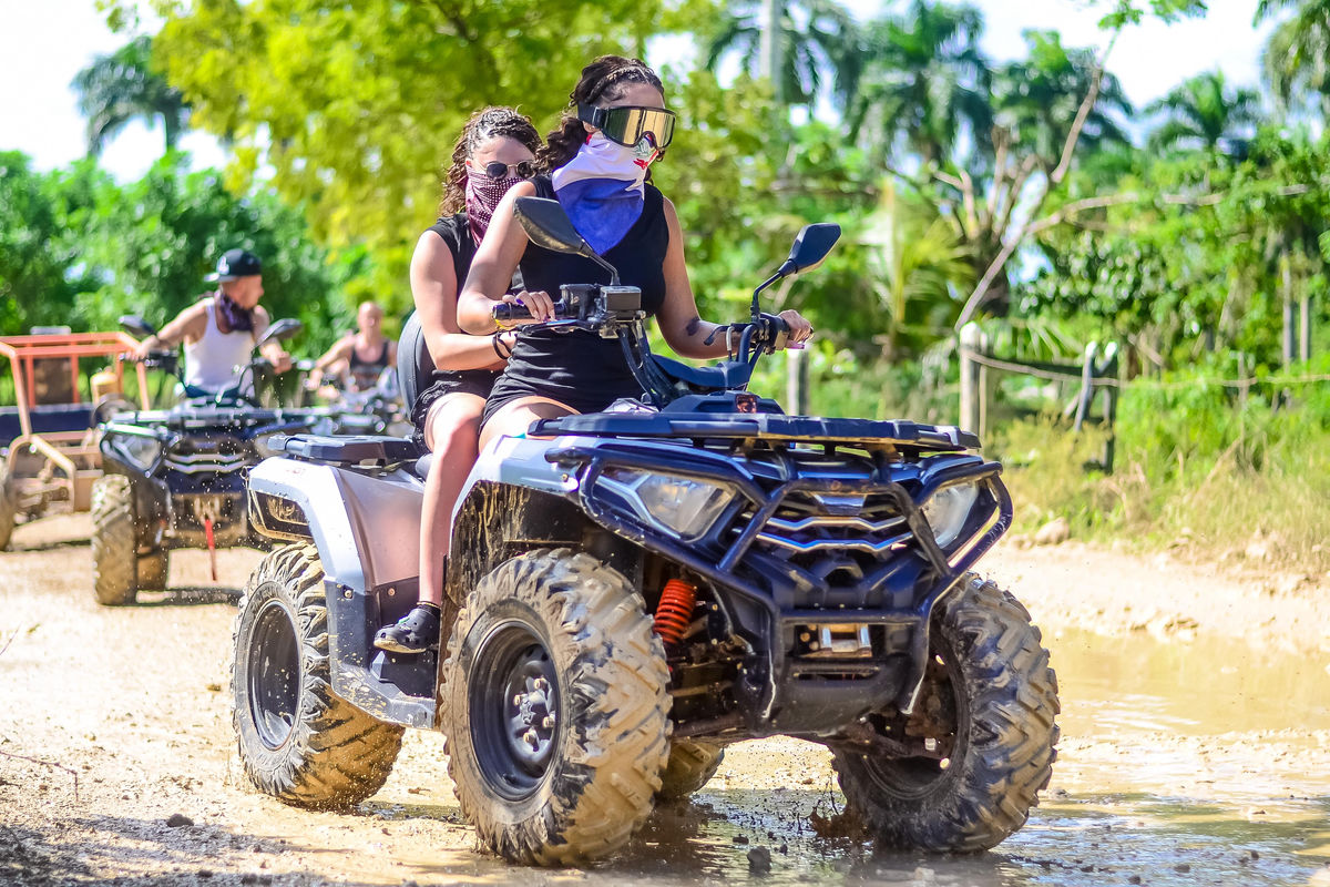 Punta Cana Two women riding an ATV with helmets and masks on a dirt trail.