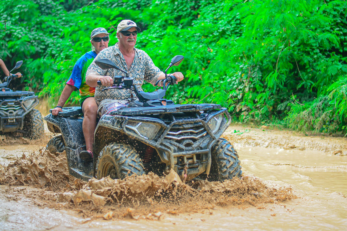 Punta Cana Two people riding an ATV through muddy trail in lush green jungle in Punta Cana.
