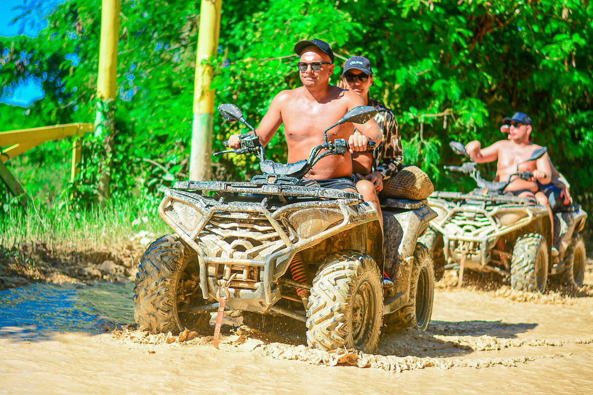 Punta Cana Group of people riding ATVs through muddy trail in lush green environment.