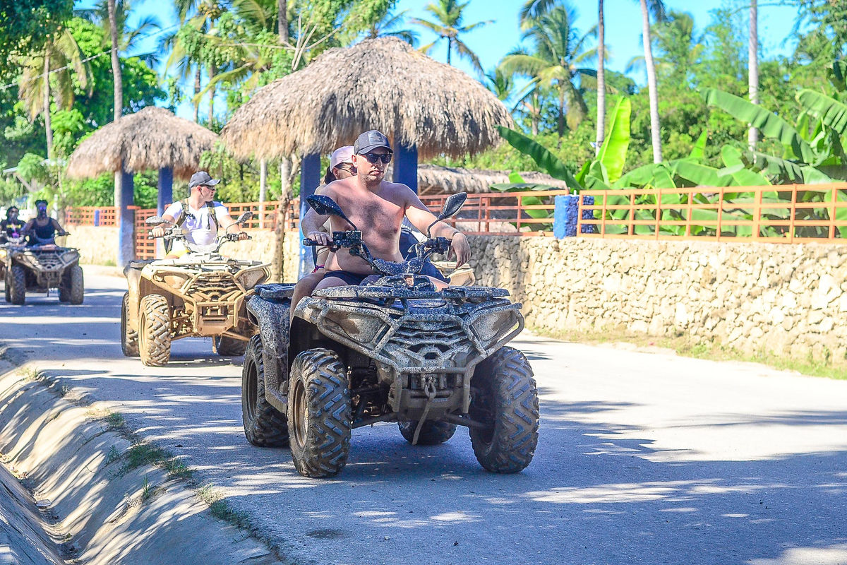 Punta Cana Man riding an ATV through a tropical area with thatched huts and lush greenery in Punta Cana.