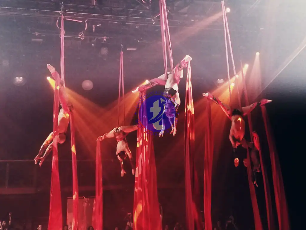 Punta Cana Performers showcase acrobatics on red silks under colorful stage lighting.