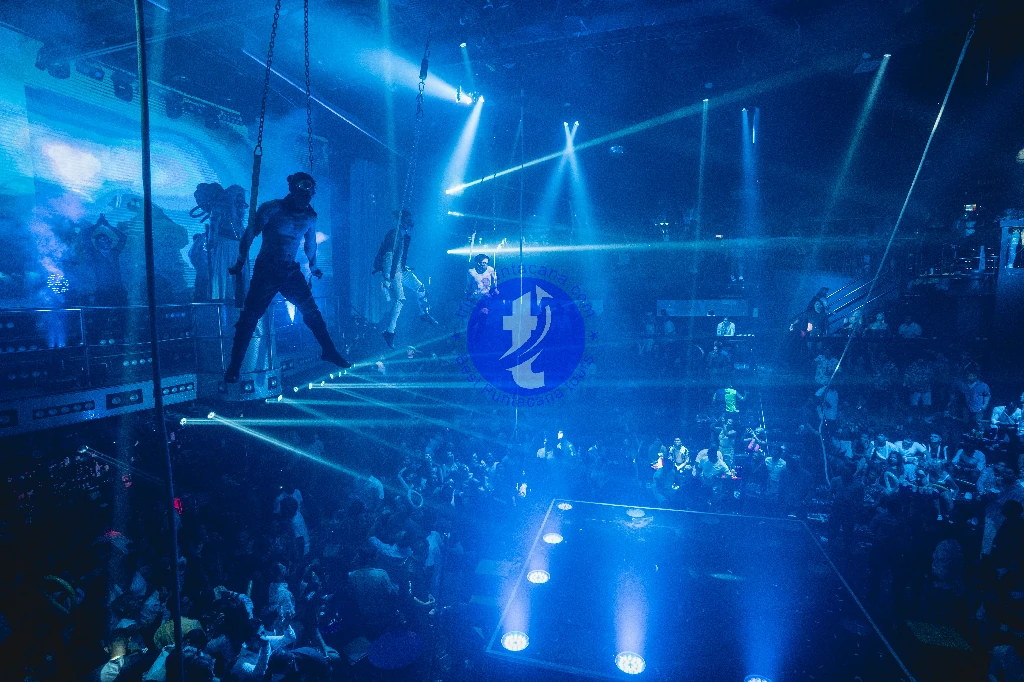 Punta Cana Performers walk on a high wire above a lively crowd in a nightclub with dynamic blue lighting.