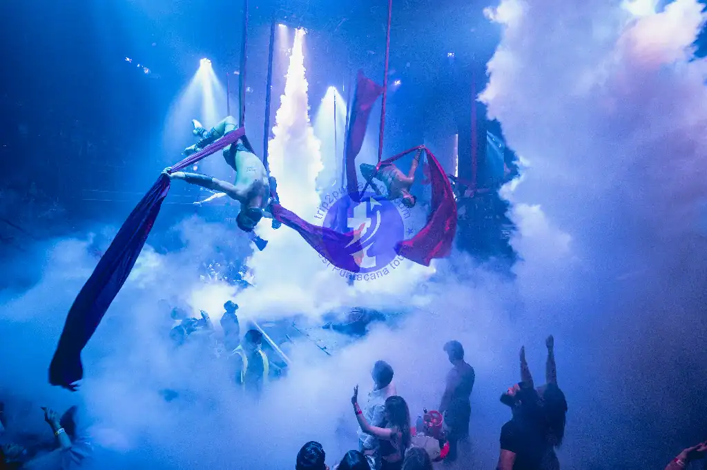 Punta Cana Aerial silk performers performing acrobatics on colorful fabrics in a foggy, illuminated stage setti.