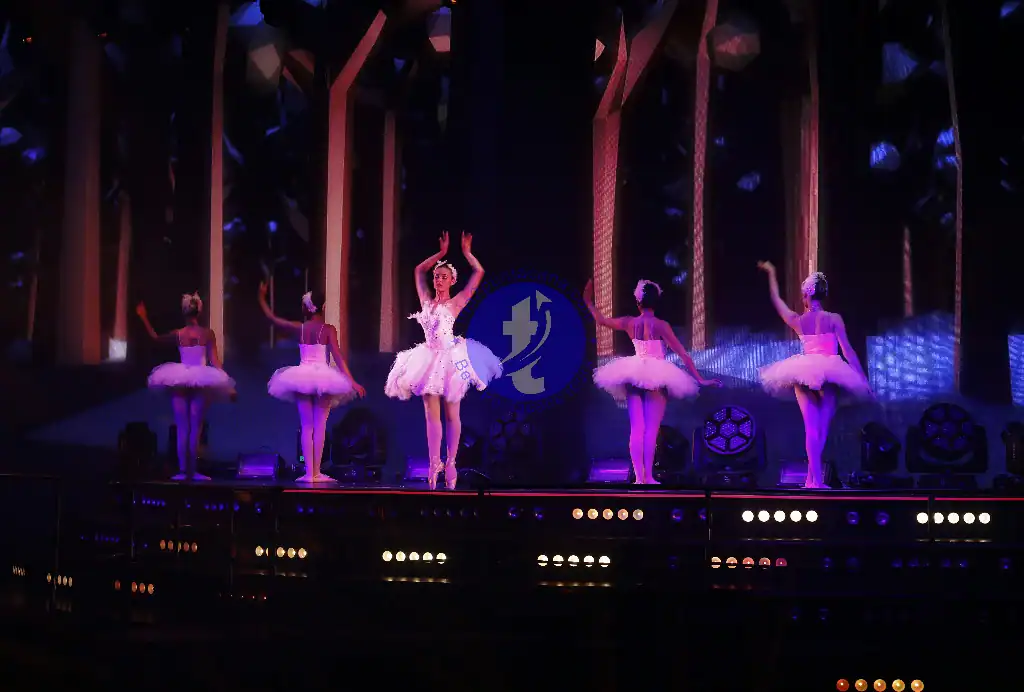 Punta Cana Ballet dancers in pink tutus performing on stage with colorful lighting.
