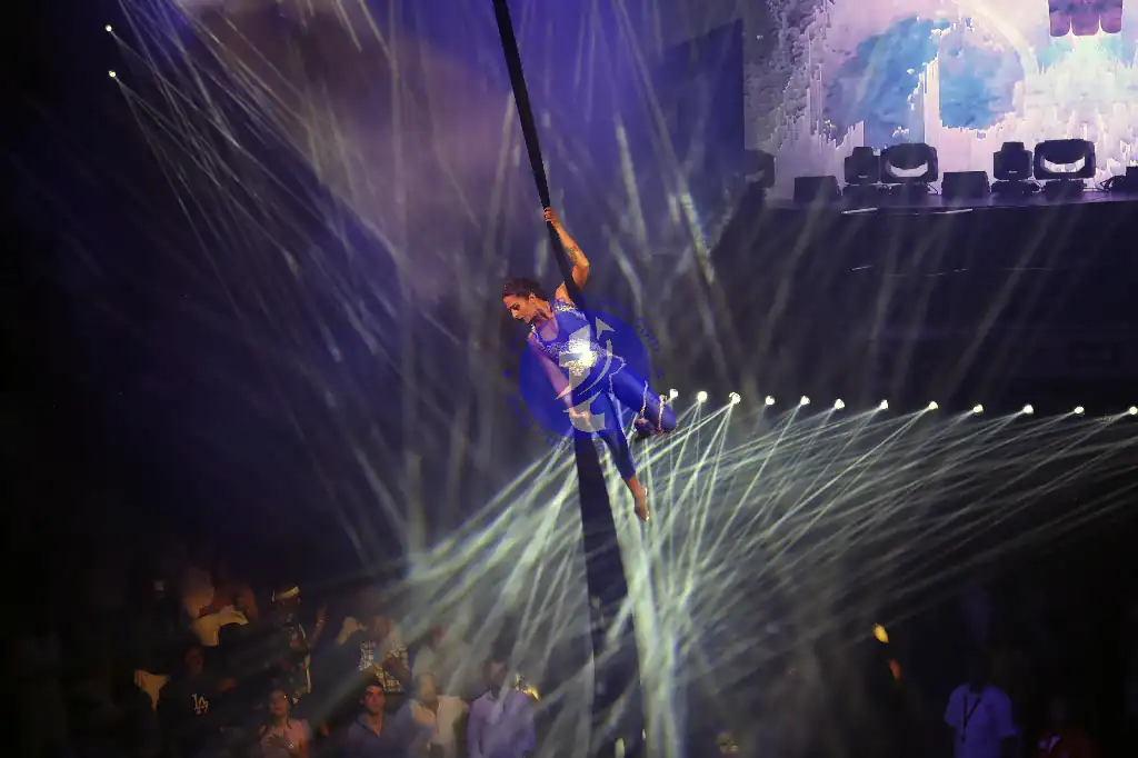 Punta Cana Performer hanging from a trapeze during a live show with vibrant stage lighting.
