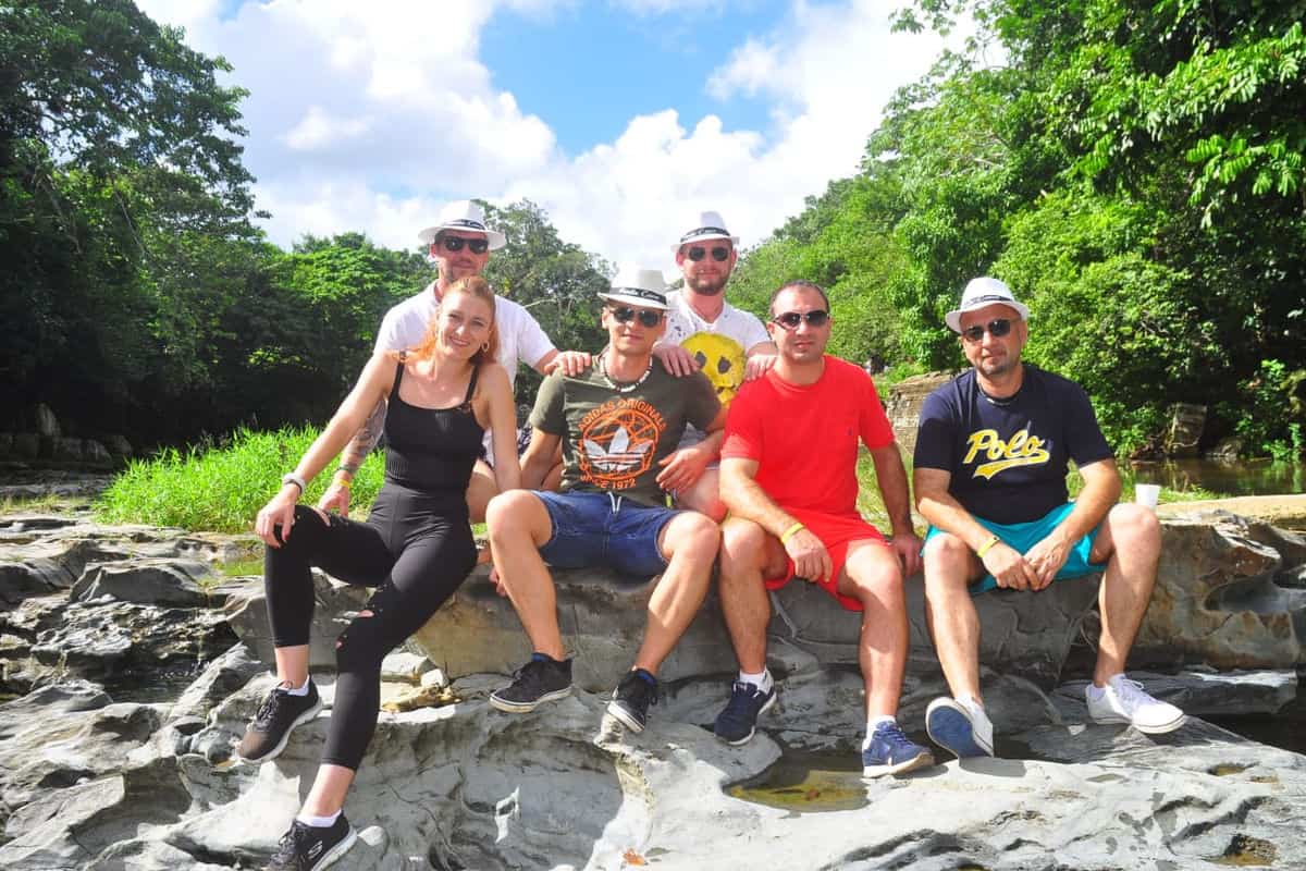 Punta Cana Group of friends relaxing on rocks near a river in lush green surroundings.