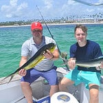 Punta Cana Fishing in Punta Cana with two men holding fish on a boat in turquoise waters.