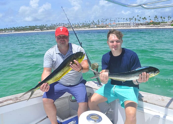 Punta Cana Fishing in Punta Cana with two men holding fish on a boat in turquoise waters.