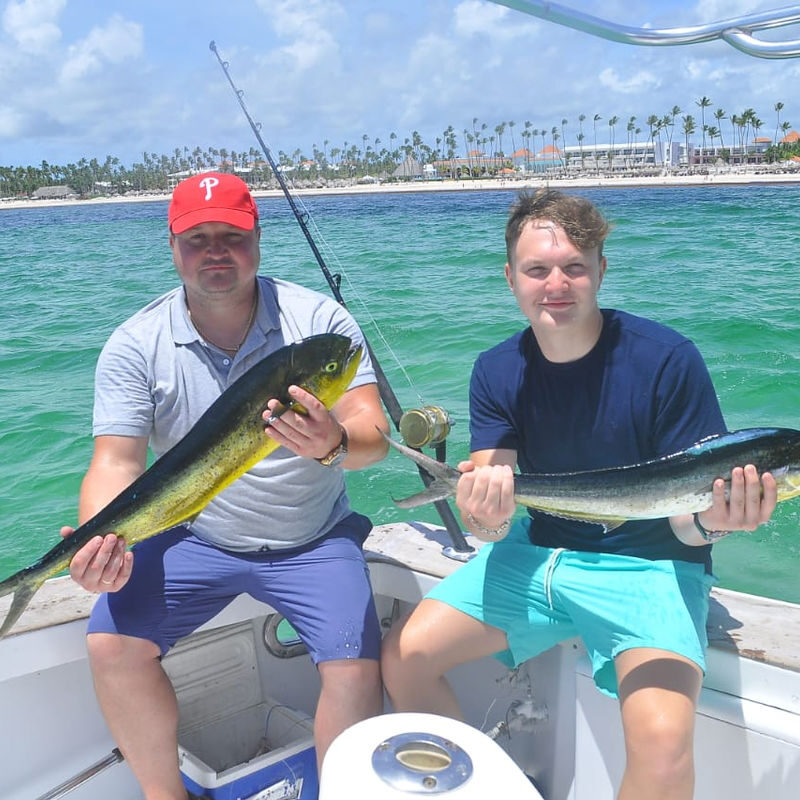 Punta Cana Fishing in Punta Cana with two men holding fish on a boat in turquoise waters.