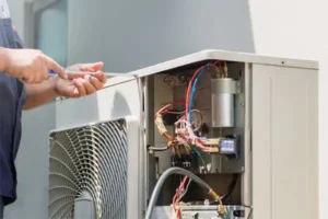 A skilled technician is diligently repairing an outdoor air conditioning unit with exposed wires, expertly using a tool, much like during a precise furnace repair.