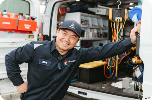 A technician in a uniform labeled "Will" stands smiling beside an open service van filled with tools and equipment.