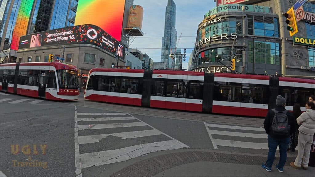 Red streetcar in downtown Toronto with digital billboards and skyscrapers.