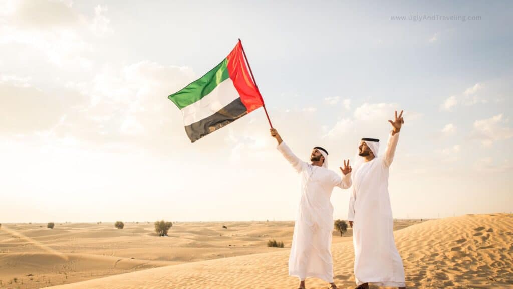 Vibrant image of two men in traditional white Emirati clothing celebrating in the Dubai desert with the UAE flag.