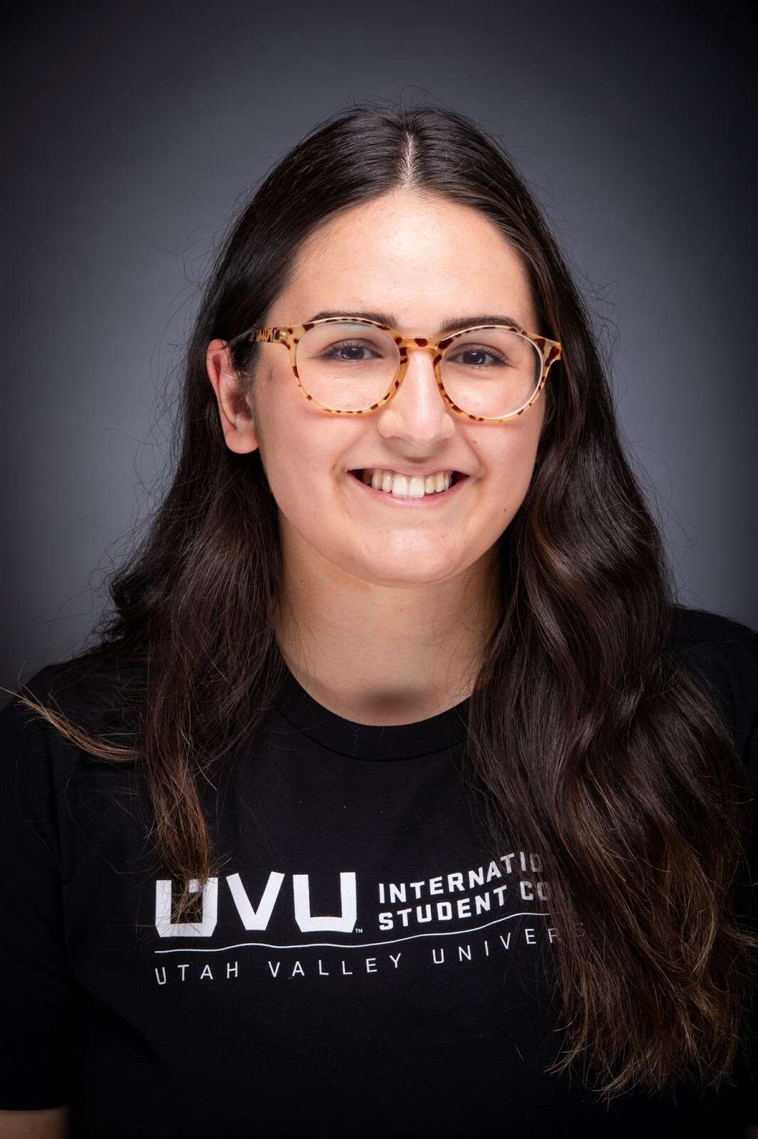 Bright smiling young woman wearing tortoiseshell glasses and a black Utah Valley University International Student Council t-shirt for UVU Review.