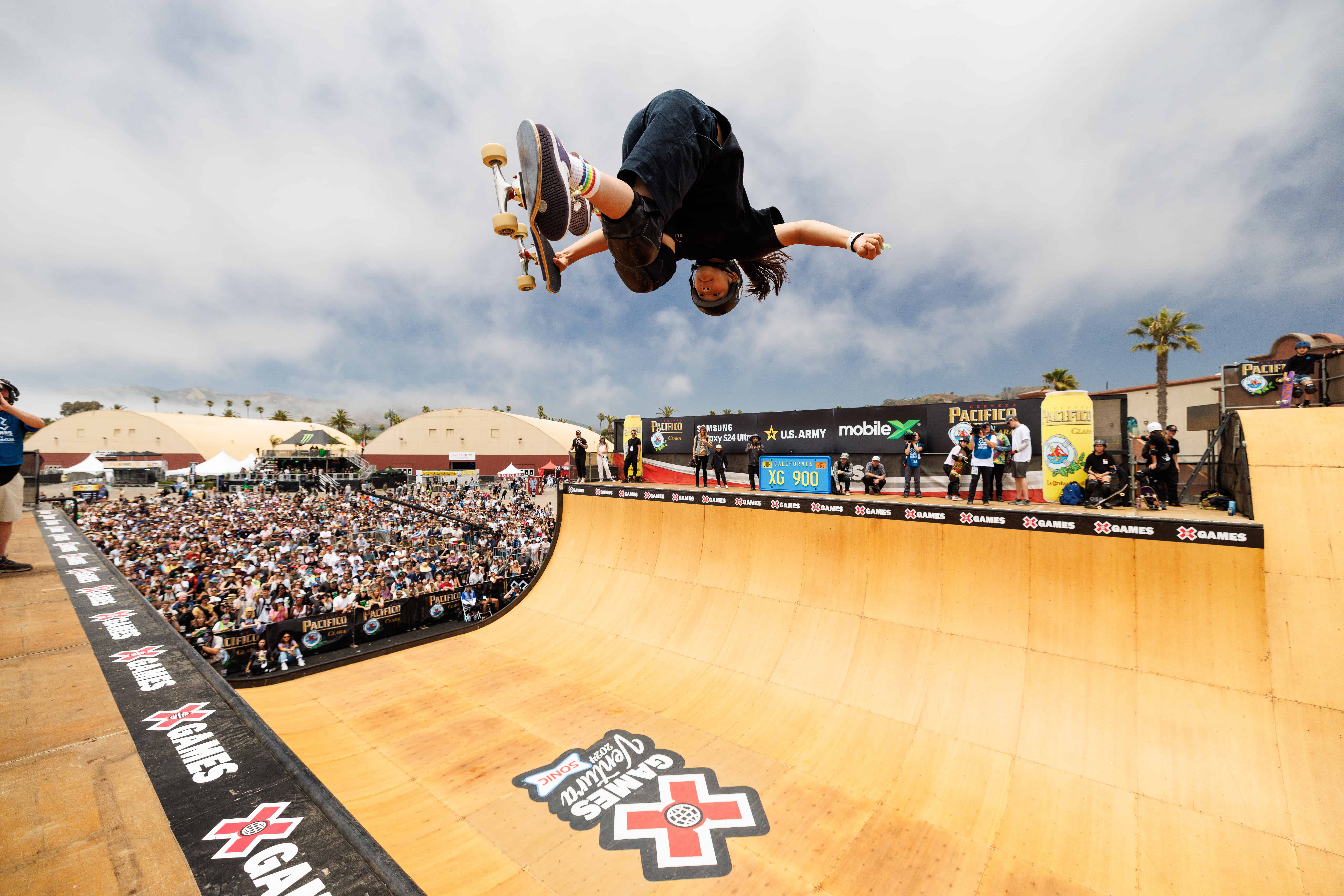 Skateboarder performing trick on vert ramp at X Games event in California.