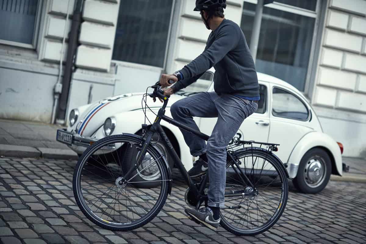 FALTER_City Falter_3745 Mann fährt Fahrrad in der Stadt mit klassischen Autos im Hintergrund.