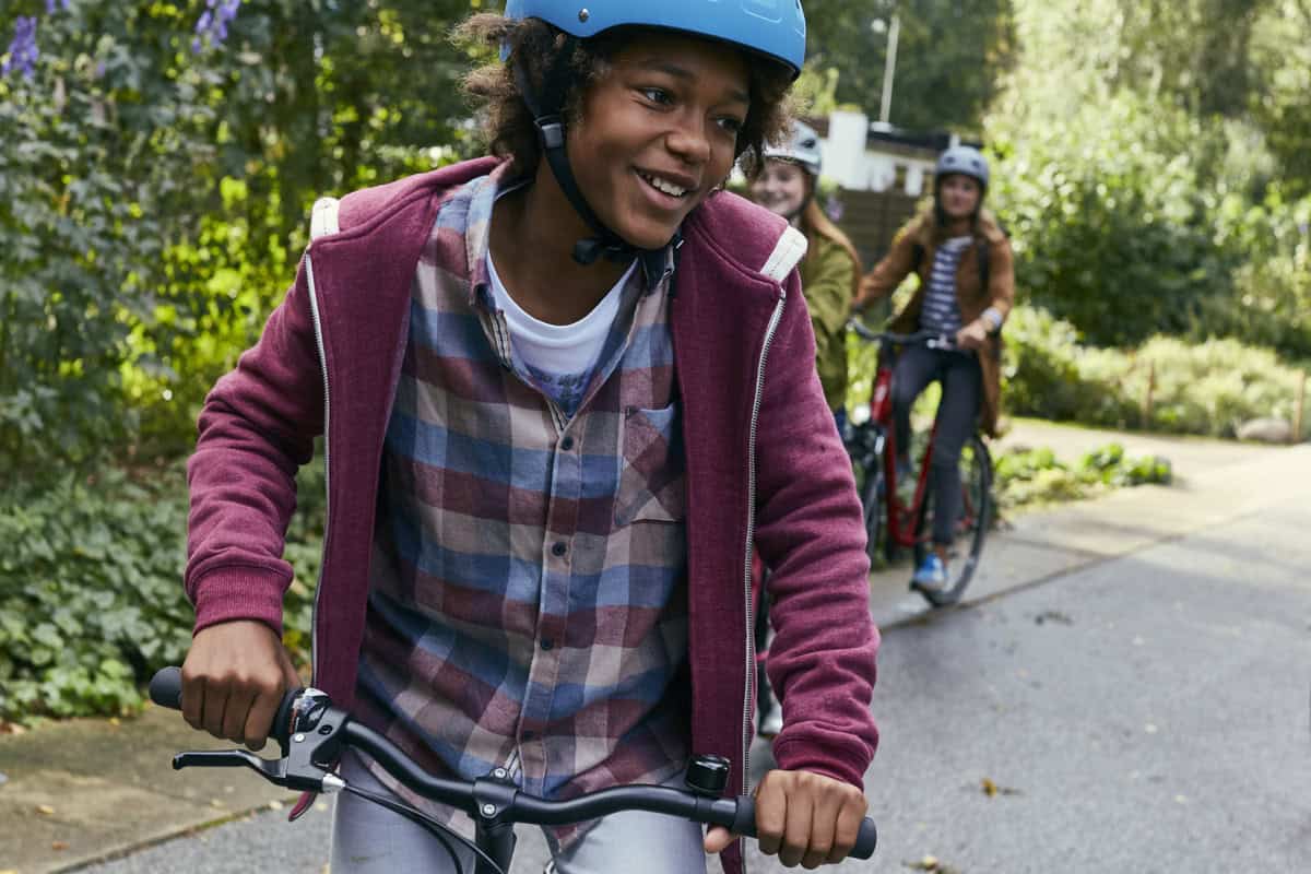 FALTER_Kids Morrison_4459 Junge Mädchen beim Fahrradfahren im Park mit Helm und Rucksack.