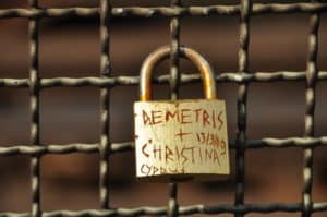 Alt: Rostiges Vorhängeschloss mit handgeschriebener Beschriftung an Metallzaun.