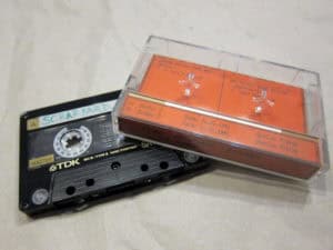 Alter Text: Vintage Audiospur-Kassette mit translucidem Gehäuse und orangefarbenem Label.
