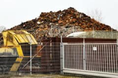 Alt text: Müllberg aus Holz und Schrott hinter Zaun und Stacheldraht.