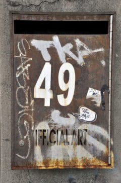 - Verschmutzte Hausnummerntafel mit Graffiti und alten Stickern, urbanes Kunstwerk.