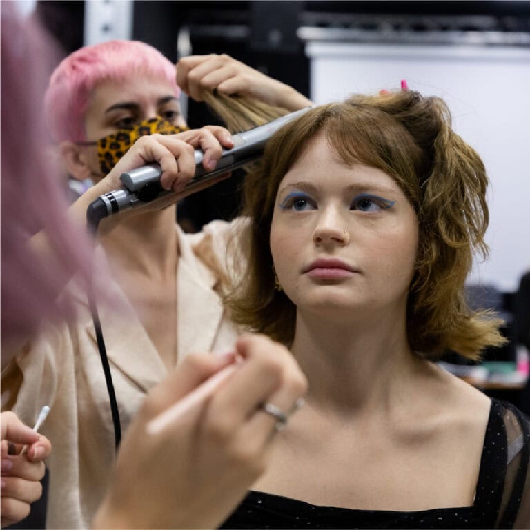 Maquilhadora profissional a trabalhar cabelos em modelo jovem olhar fashion.