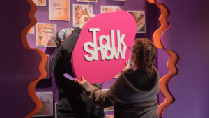 Pessoas interagindo com sinalização de "Talk Show" em ambiente de aprendizagem visual moderno.