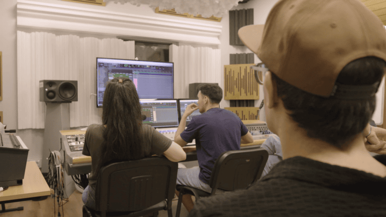 Estudantes em estúdio de gravação, aprendendo produção musical com equipamentos profissionais.