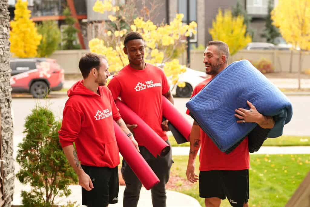 Three movers in red YEG Edmonton Movers hoodies with moving gear outdoors.