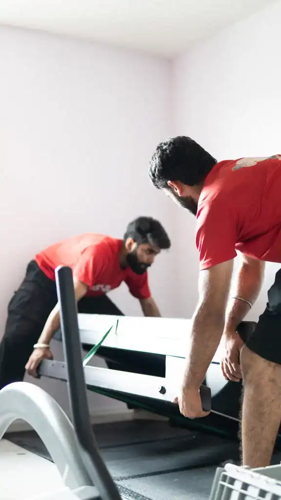Two movers lifting a piano with heavy equipment in a home setting.